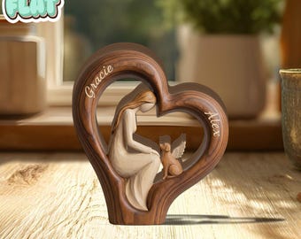 Può includere: Scultura in legno a forma di cuore con una donna e un cane con le ali d'angelo. La scultura è marrone con una figura beige chiaro di una donna e un cane. I nomi "Gracie" e "Alex" sono incisi sul cuore.