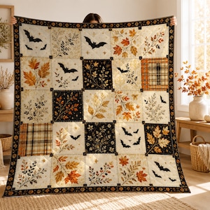 Könnte beinhalten: Ein quadratischer Patchwork-Quilt mit einem sich wiederholenden Raster aus abwechselnden Blöcken. Das Design umfasst cremefarbene, schwarze und orangefarbene Quadrate, die mit fliegenden Fledermaussilhouetten, herbstlichen Blättern und Karomustern verziert sind.