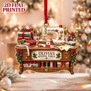 May include: A 2D flat printed hanging ornament featuring a sewing table with a sewing machine, fabric stacks, scissors, thread spools, and a measuring tape. The table has a sign that reads OLIVIA'S SEWING TABLE with holly and a heart.