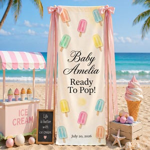 May include: A beach-themed baby shower banner with the text "Baby Amelia Ready To Pop!" and colorful popsicle illustrations. A pink ice cream cart and a large ice cream cone are also visible.