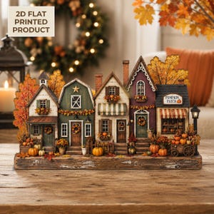 May include: A 2D flat printed tabletop decoration featuring a row of five miniature autumn-themed buildings. The scene includes houses in green, white, and purple with orange pumpkins, fall foliage, and a sign that reads Pumpkin Patch.