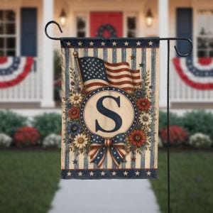 May include: A garden flag with an American flag design and a large letter "S" in a circular emblem. The flag has a vintage aesthetic, with floral elements and a bow. It's displayed on a black metal stand, suitable for outdoor decoration.