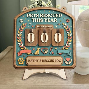 May include: Wooden pet rescue log with the text "PETS RESCUED THIS YEAR" and "KATHY'S RESCUE LOG". The teal background features paw prints, hearts, and a ribbon. The counter displays "000".