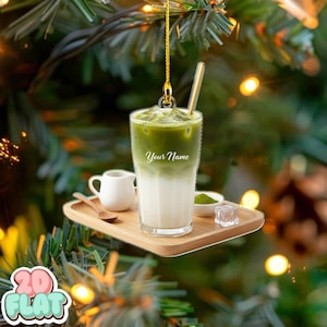 Könnte beinhalten: Ein klarer Acrylschmuck in Form eines Matcha Latte. Der Schmuck zeigt ein geschichtetes grünes und weißes Getränk mit Strohhalm, einem kleinen Sahnekännchen und einem Holztablett mit Matcha-Pulver und Eiswürfeln. Der Text "Your Name" steht auf dem Glas.