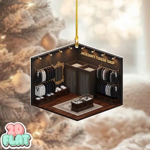 Könnte beinhalten: Ein sechseckiger Christbaumschmuck, der einen Miniatur-Smoking-Shop-Innenraum zeigt. Der Shop hat Kleiderständer mit Anzügen, eine Vitrine und einen Spiegel. Der Text "JACKSON'S TUXEDO SHOP" ist oben zu sehen. Der Schmuck wird von einem goldenen Faden gehalten.