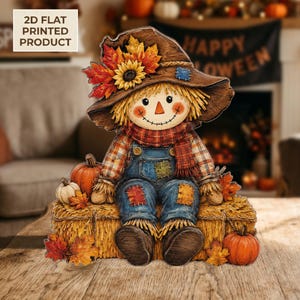 May include: A 2D flat printed scarecrow decoration sitting on a hay bale. The scarecrow wears a brown hat with autumn leaves and a sunflower, a plaid shirt, and blue overalls with patches. Orange pumpkins and fall foliage surround the base.