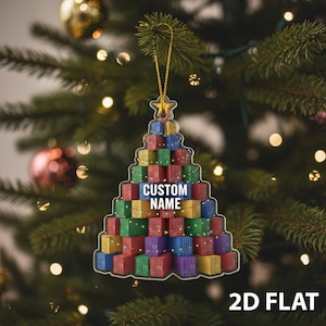 May include: A Christmas tree ornament shaped like a tree made of colorful shipping containers. The ornament has a gold star at the top and the text "CUSTOM NAME" in the center. The words "2D FLAT" are at the bottom.