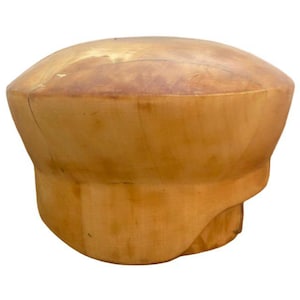 May include: A light brown wooden hat block with a rounded top and a wide brim. The hat block is made of solid wood and has a natural finish. The hat block is used for shaping hats.