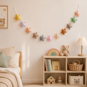 Colorful felt star garland for nursery wall decor with pastel rainbow stars hanging on string, baby room decoration above crib or shelf, soft Montessori nursery decor perfect for kids room and baby shower gift.