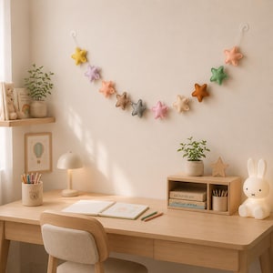 Colorful felt star garland for nursery wall decor with pastel rainbow stars hanging on string, baby room decoration above crib or shelf, soft Montessori nursery decor perfect for kids room and baby shower gift.