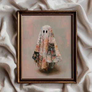 Könnte beinhalten: Ein gerahmter Kunstdruck, der eine Geisterfigur zeigt, die in eine Patchwork-Decke aus verschiedenen Blumenmustern in Rosa-, Creme- und gedämpften Grüntönen gehüllt ist, mit zwei einfachen schwarzen ovalen Augen vor einem weichen, hellen Hintergrund.