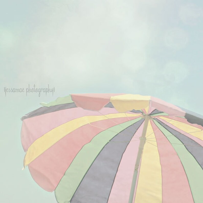 Peut inclure: Un parasol de plage ray&eacute; color&eacute; avec un sch&eacute;ma de couleurs pastel. Le parasol est ouvert et le haut est visible contre un ciel bleu clair.