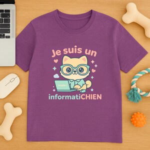以下が含まれることがあります： メガネをかけた漫画の猫がラップトップで作業している紫色のTシャツ。シャツのテキストはピンクと青で「Je suis un informatiCHIEN」と書かれています。シャツは犬のおもちゃとコンピューターに囲まれています。