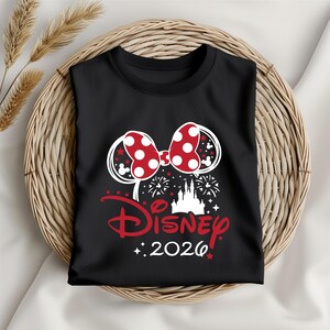 May include: Black t-shirt featuring a red and white polka dot bow design, with the word "Disney" in red script and the year "2026". The design includes a castle silhouette and fireworks.