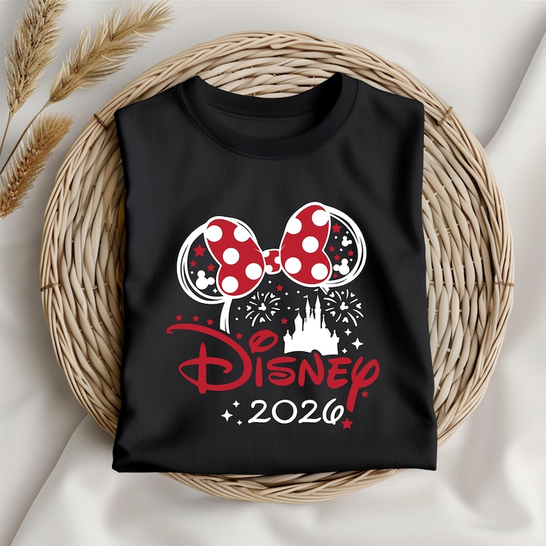 May include: Black t-shirt featuring a red and white polka dot bow design, with the word "Disney" in red script and the year "2026". The design includes a castle silhouette and fireworks.