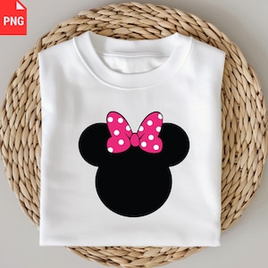K&ouml;nnte beinhalten: Wei&szlig;es Sweatshirt mit Rundhalsausschnitt und schwarzer Maus-Kopf-Silhouette und rosa Schleife. Die Schleife hat wei&szlig;e Tupfen. Das Sweatshirt ist auf einer gewebten, hellbraunen Oberfl&auml;che gefaltet.