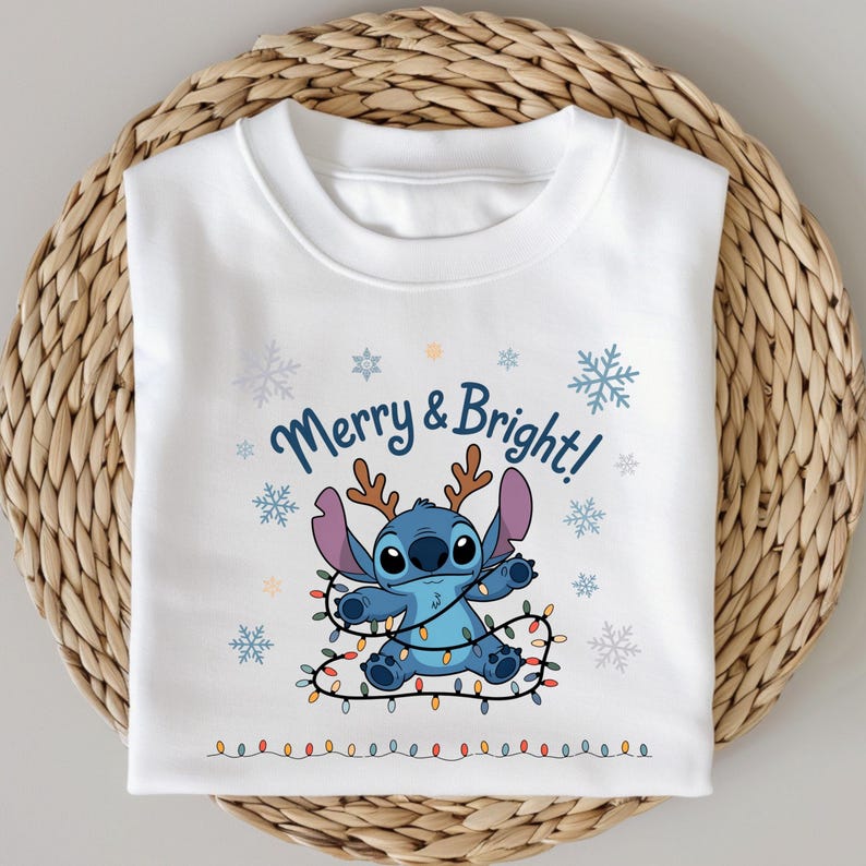Pu&ograve; includere: Felpa bianca con un personaggio blu dei cartoni animati con le corna e una fila di luci colorate. Il testo "Merry & Bright!" &egrave; sopra il personaggio, con fiocchi di neve intorno. La felpa &egrave; piegata su una superficie tessuta.