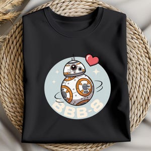 May include: Black crew neck t-shirt featuring a cartoon BB-8 droid design. The design includes a light blue circle with the droid, a red heart, and the text "BB-8". The droid is white, orange, and silver.