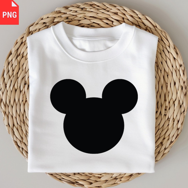 K&ouml;nnte beinhalten: Ein wei&szlig;es Sweatshirt mit einer gro&szlig;en schwarzen Mickey Mouse Silhouette. Das Sweatshirt ist gefaltet und auf einem gewebten, runden Platzdeckchen platziert. Das Design ist einfach und k&uuml;hn, ideal f&uuml;r Fans der ikonischen Figur.