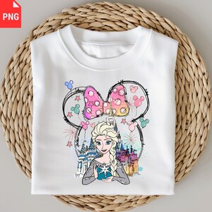 May include: White sweatshirt featuring a colorful graphic of Elsa from Frozen, a pink polka-dot bow, and a castle. The design includes Mickey Mouse ears and colorful fireworks. The sweatshirt is displayed on a woven basket.