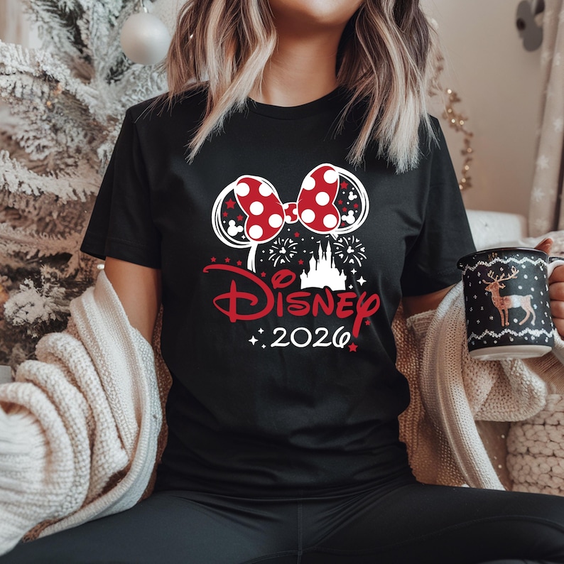 May include: Black t-shirt featuring a red and white polka dot bow, Mickey Mouse ears, and the word "Disney" in red script. The design includes a castle, fireworks, and the year "2026".