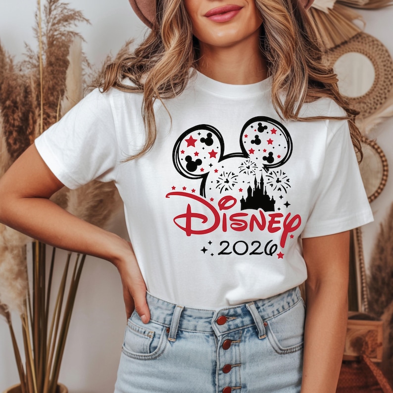 May include: White t-shirt featuring a Mickey Mouse design with red stars and the text "Disney 2026". The design includes a silhouette of a castle and fireworks.