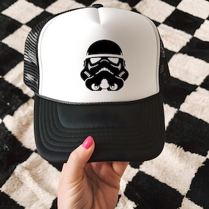 May include: Black and white trucker hat featuring a Stormtrooper helmet design. The hat has a black brim and mesh back, with a white front panel displaying the helmet graphic. A stylish accessory for fans of the iconic sci-fi franchise.