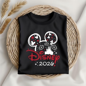 May include: Black t-shirt featuring a Disney design. The design includes Mickey Mouse ears filled with red stars and white Mickey heads, fireworks, a castle, and the word "Disney" in red with the year "2026".