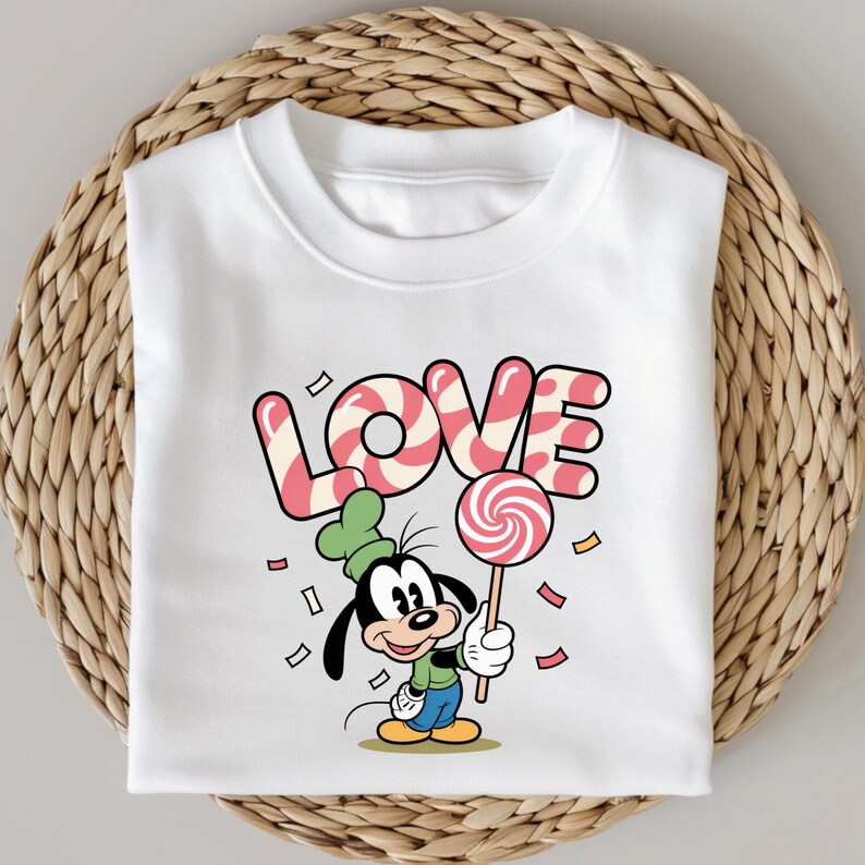 May include: White sweatshirt featuring a cartoon character holding a lollipop. The word "LOVE" is written in pink and white candy cane-striped letters. The character is wearing a green hat and holding a red and white swirled lollipop.
