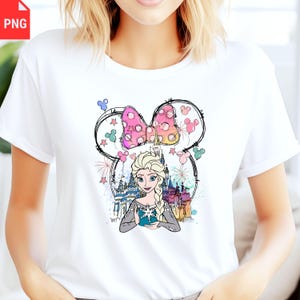 May include: White t-shirt featuring a cartoon illustration of Elsa from Frozen. The design includes a pink polka-dot bow, a castle, and fireworks. The artwork is framed by a Mickey Mouse-style outline.