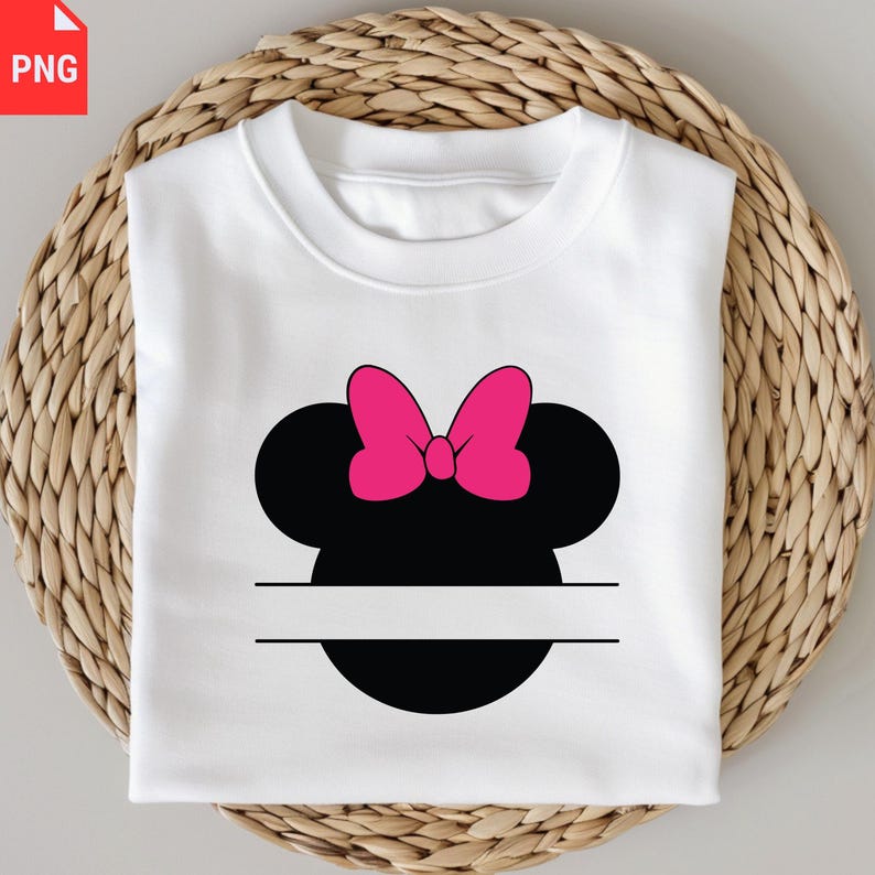 K&ouml;nnte beinhalten: Wei&szlig;es Sweatshirt mit einem schwarzen Minnie-Mouse-Kopf-Design und einer leuchtend rosa Schleife. Das Design enth&auml;lt einen horizontalen Freiraum unter dem Kopf, ideal f&uuml;r die Personalisierung. Das Sweatshirt ist auf einer gewebten, hellbraunen Oberfl&auml;che gefaltet.