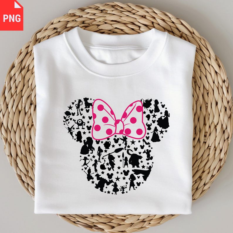 K&ouml;nnte beinhalten: Wei&szlig;es Sweatshirt mit einem Minnie-Mouse-Design. Die Silhouette ist mit schwarzen Charakterumrissen und Sternen gef&uuml;llt, mit einer rosa Schleife mit Punkten. Das Sweatshirt ist auf einer gewebten, hellbraunen Oberfl&auml;che gefaltet.