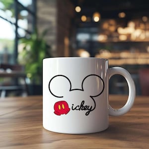 May include: White ceramic mug featuring a black outline of Mickey Mouse's head and ears, with a red and yellow glove and the word "ickey" in a script font. The mug has a white handle and is set on a wooden surface.