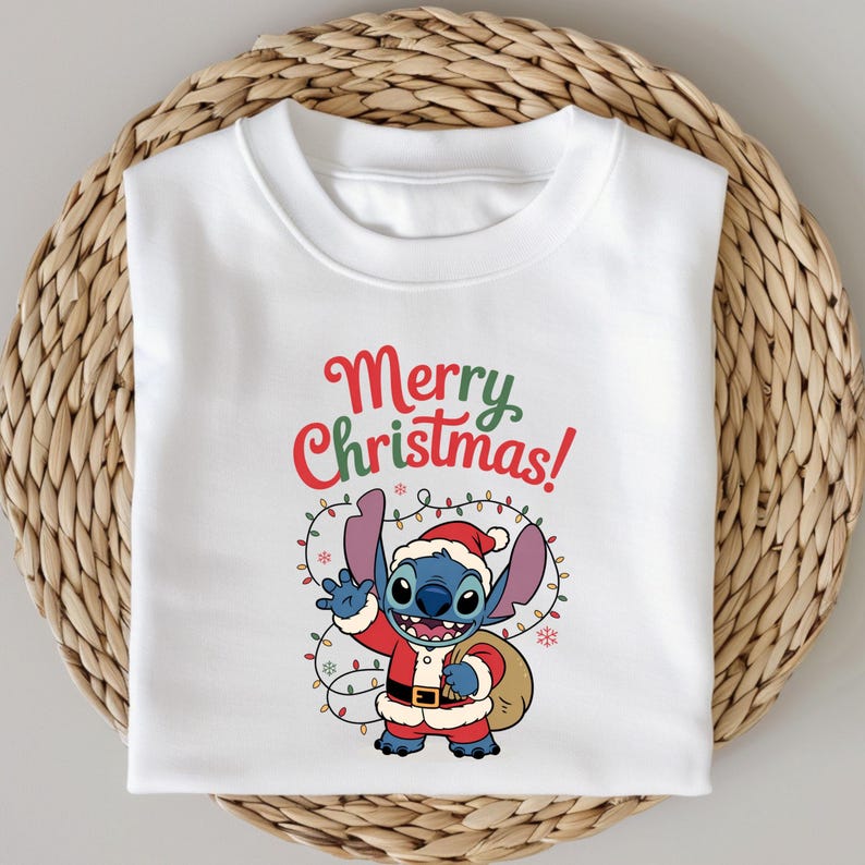 Pu&ograve; includere: Felpa bianca con un personaggio dei cartoni animati vestito da Babbo Natale, che tiene un sacco e saluta. Le parole "Merry Christmas!" sono scritte sopra il personaggio in rosso e verde. Il personaggio &egrave; blu con grandi orecchie e indossa un cappello e un costume da Babbo Natale.