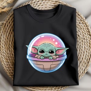 May include: Black long-sleeve shirt featuring a cartoon illustration of a green alien-like character in a clear bubble. The character has large eyes and ears, with a pink and purple background inside the bubble.