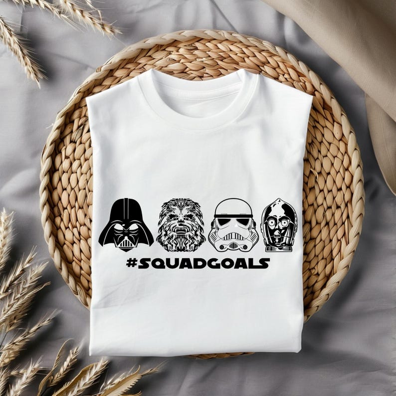May include: White t-shirt featuring black and white illustrations of Star Wars characters Darth Vader, Chewbacca, a Stormtrooper, and C-3PO. The text "#SQUADGOALS" is printed below the characters.