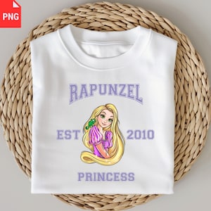 Peut inclure: Sweat-shirt blanc avec un graphisme de Raiponce, un caméléon vert et le texte "RAPUNZEL PRINCESS EST 2010" en violet. Le sweat-shirt est plié sur une surface tissée.