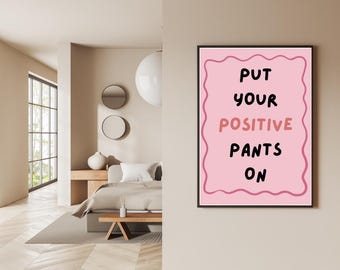 Può includere: Un poster rosa incorniciato con le parole "PUT YOUR POSITIVE PANTS ON" in lettere nere e rosa. Il poster è appeso a una parete beige in una camera da letto. La stanza ha un letto, una finestra e specchi decorativi.