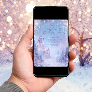 May include: A smartphone displays a birthday party invitation. The invitation features a winter wonderland scene with a castle, trees, and falling snow. Text reads "Sophie's 1st Birthday Party" with event details. The background is a snowy landscape.