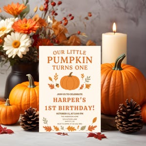 Puede incluir: Una tarjeta de invitación con el texto "Our Little Pumpkin Turns One" y "Harper's 1st Birthday!" está rodeada de calabazas, flores, una vela encendida y piñas. El diseño de la tarjeta incluye una ilustración de calabaza y hojas de otoño.