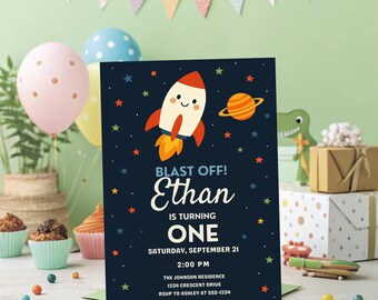 Könnte beinhalten: Eine marineblaue Geburtstagseinladung mit einer Raketenillustration und dem Text "BLAST OFF! Ethan wird EINS." Die Einladung enthält Datum, Uhrzeit und Ort. Bunte Luftballons und Partydekorationen sind im Hintergrund.