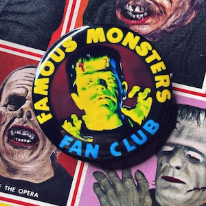 May include: A round black button with the text "FAMOUS MONSTERS FAN CLUB" in yellow and blue. The button features a green and yellow image of Frankenstein's monster. The background includes images of classic movie monsters.