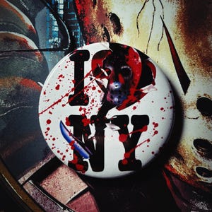 May include: A white button with the words "I NY" in black, with a graphic of a hockey mask and a knife. Red blood splatter accents the design. The button is a horror-themed collectible.