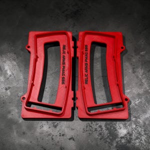 May include: Two red, rectangular objects with the text "RELIC ARMS PMAG 556" printed vertically. The objects have a frame-like design with rounded corners and small holes. The background is a dark, textured surface.