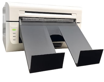 May include: A white and gray printer with black output trays. The printer has a series of indicator lights on the side. The output trays are angled downward.