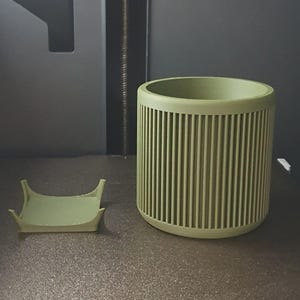 May include: A light green cylindrical container with vertical grooves and a matching small tray. The container is a solid color and has a rounded top. The tray is square with curved edges. The items appear to be 3D printed.