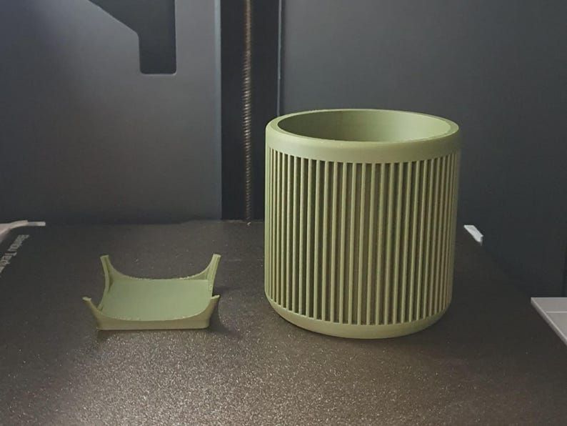 May include: A light green cylindrical container with vertical grooves and a matching small tray. The container is a solid color and has a rounded top. The tray is square with curved edges. The items appear to be 3D printed.