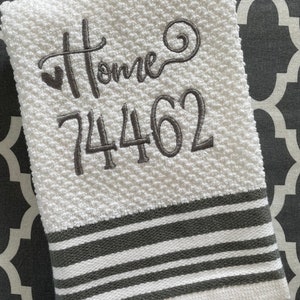 May include: White kitchen towel with gray stripes and embroidered text "Home" and the number "74462".