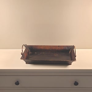 Peut inclure: Un plateau rectangulaire en métal de style antique avec une finition marron foncé et des poignées incurvées. Le plateau est posé sur une commode blanche. Ce plateau décoratif convient au service ou à l'exposition.