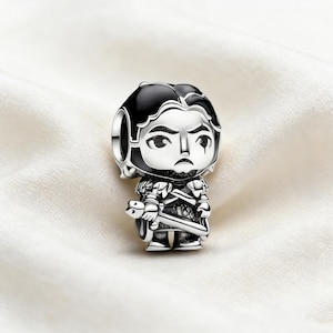 Könnte beinhalten: Ein silberner Charm, der eine stilisierte Figur mit schwarzen Haaren und Rüstung darstellt, die ein Schwert hält. Der Charm hat ein detailliertes Design mit einem strengen Gesichtsausdruck. Der Charm ist wahrscheinlich aus Sterlingsilber und ein Sammlerstück.